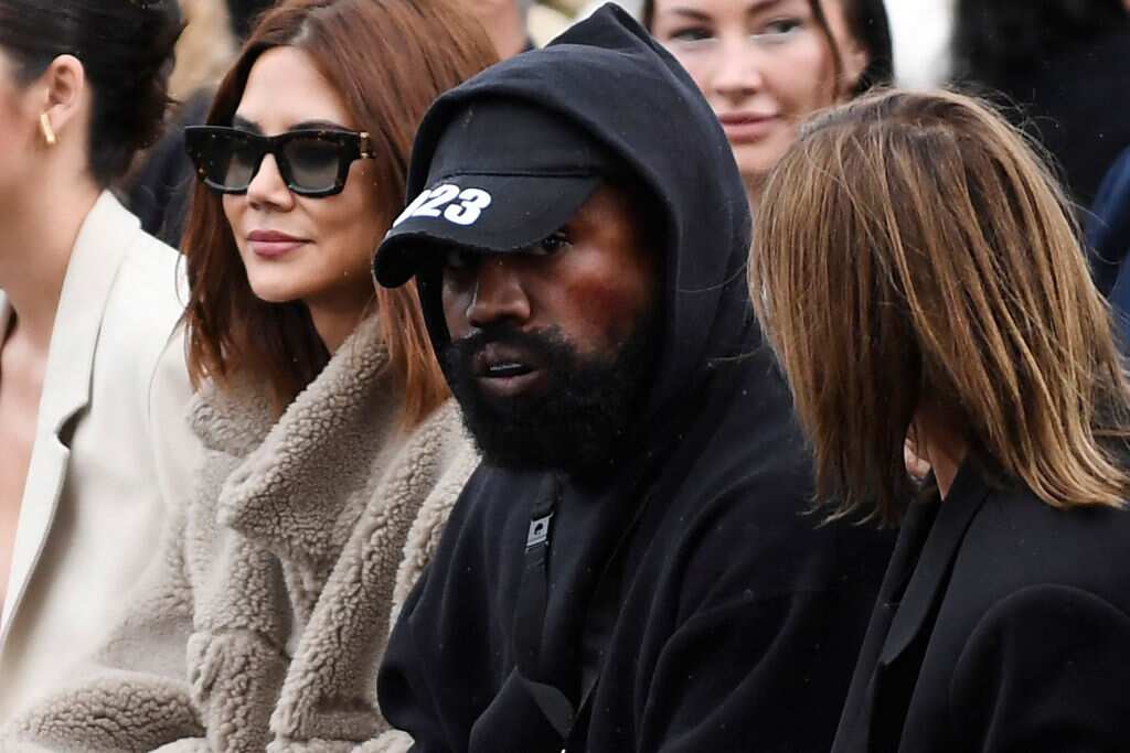 Kanye West wearing a black hooded top and cap sitting with others