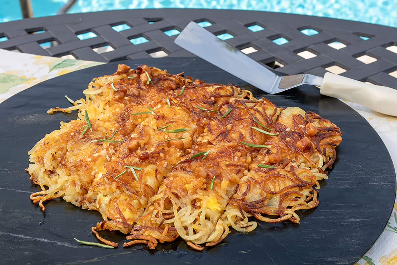 A golden-brown crisp-looking layer of spiralised potato rosti sits on a round black platter. 