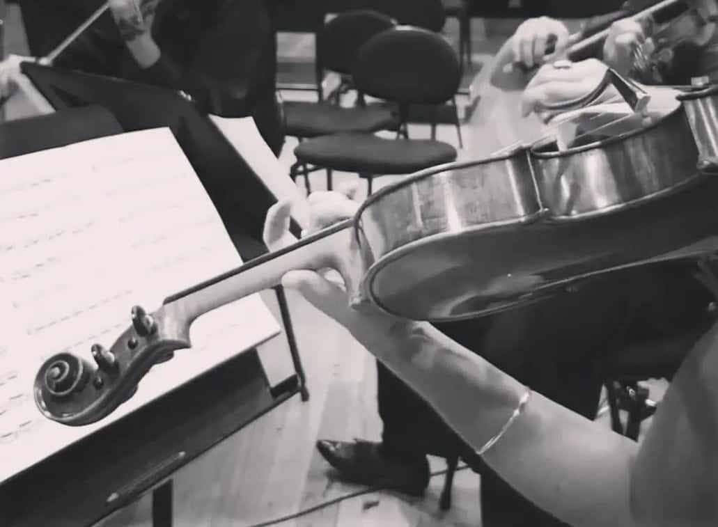 Woman playing violin in front of sheet music with an orhcestra
