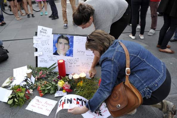 A woman kneels in front of flowers, candles and a picture of a man