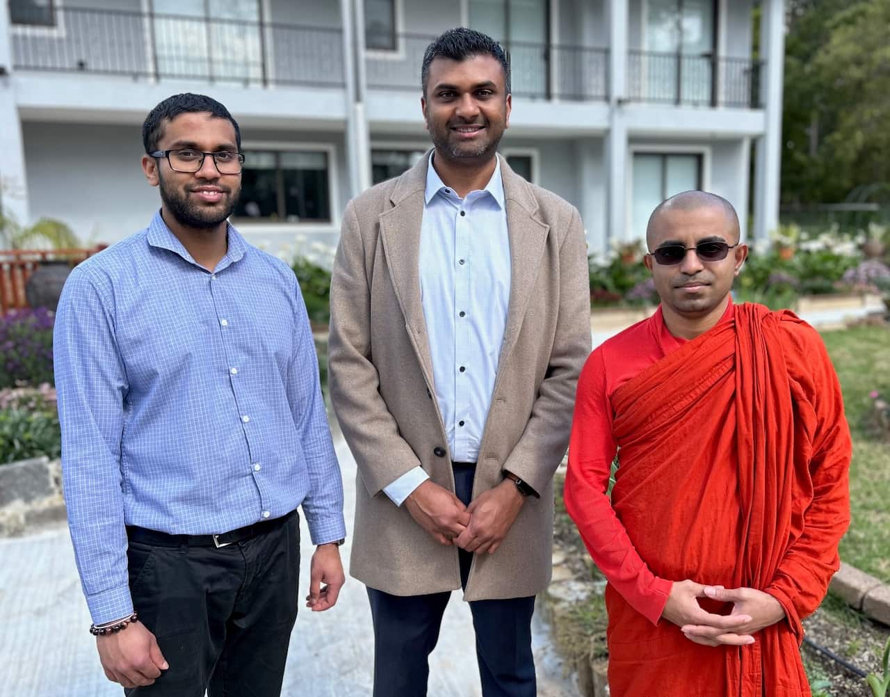Thee men stand on a pathway facing the camera.