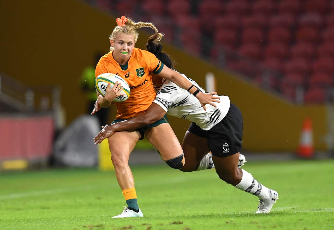 A woman in a gold rugby shirt tackled by a woman in white and black rugby uniform.