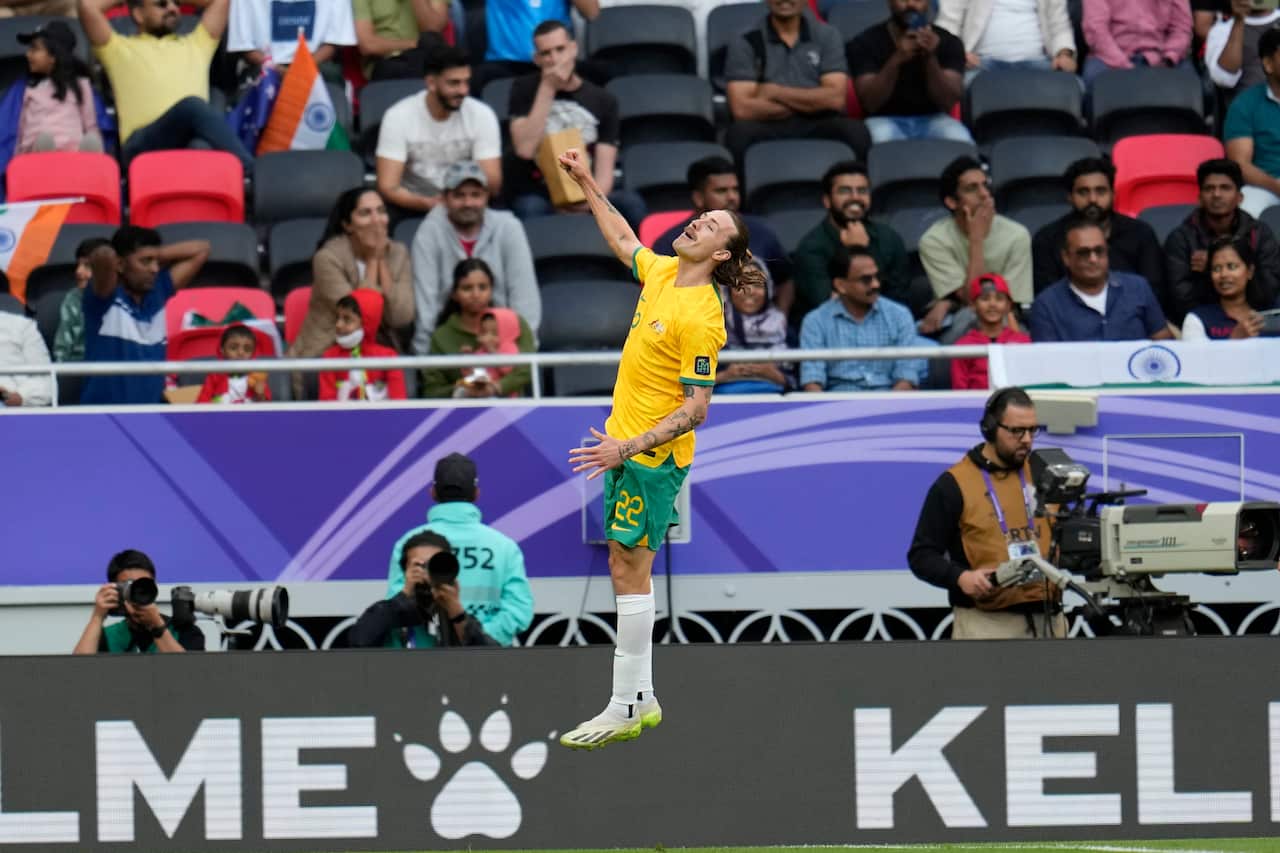 A football player in yello jersey jumps up to celebrate scoring a goal.