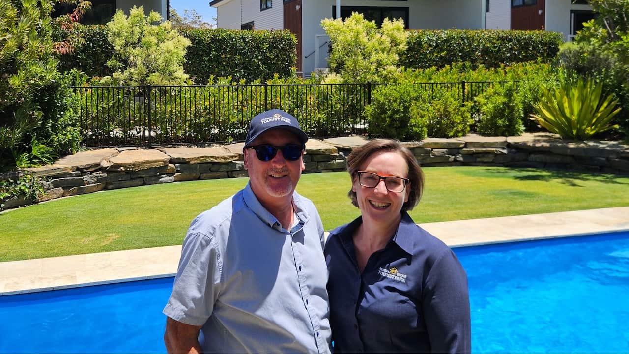 a middle aged couple smile in front of a swimming pool
