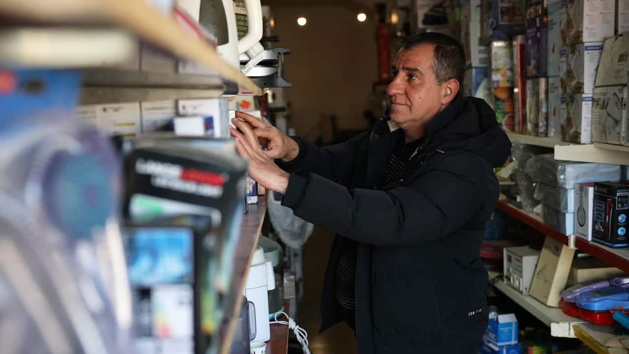 A middle-aged man in a black parka looks at shelves stocked with goods