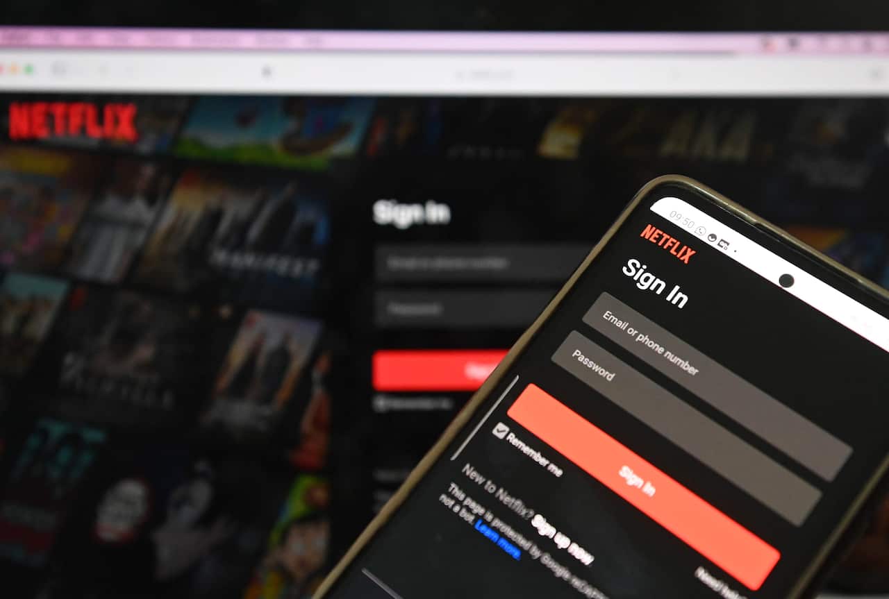 A photo of a mobile phone signing into Netflix' homepage, in front of a we browser also on Netflix's sign in page.