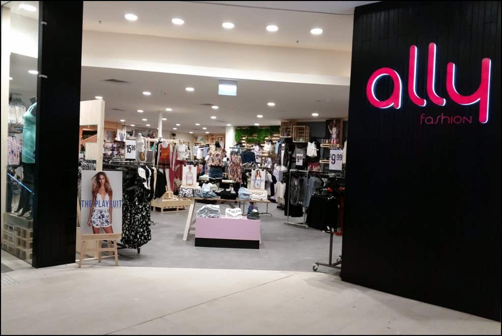 The entrance to a clothing store with a black feature wall. The word ally in pink text is lit up on the wall