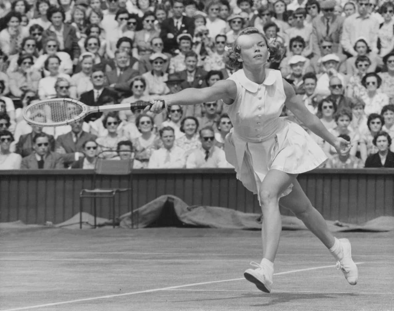 Black and white image of a woman hitting a tennis ball with a racquet. 