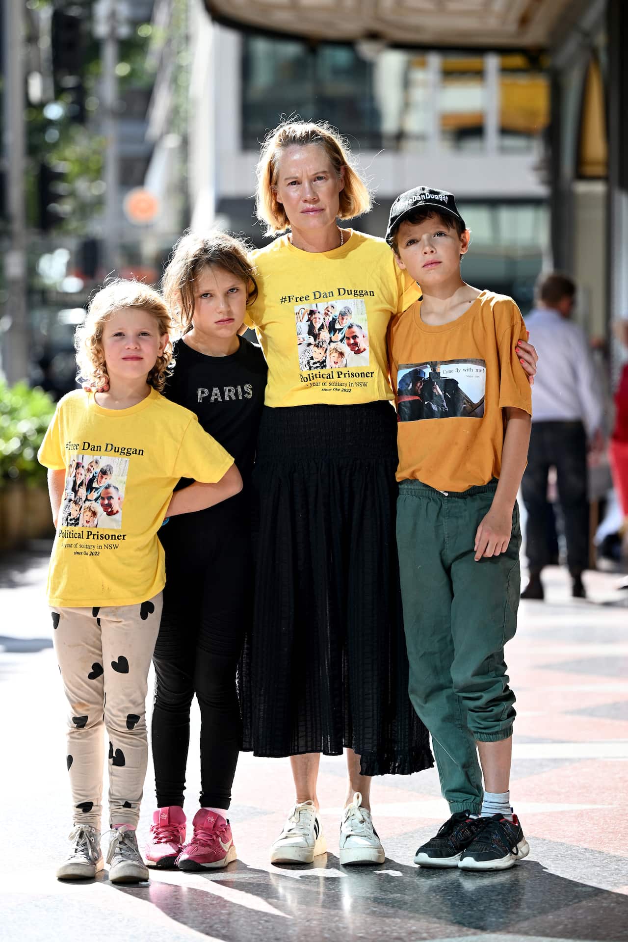 A woman wearing a yellow T-shirt and black skirt with her three children.