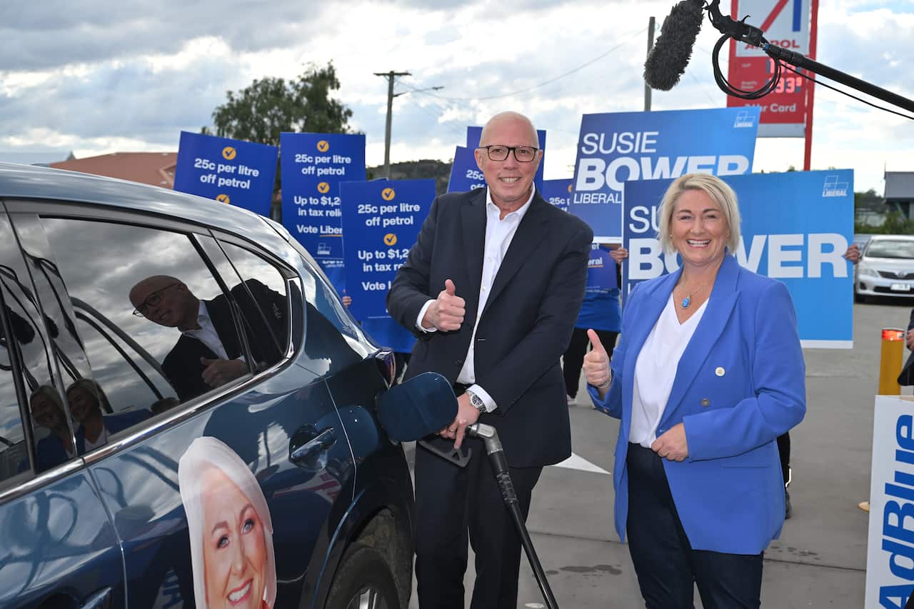 Peter Dutton gives a thumbs up while filling a car with petrol and standing next Susie Bower. 