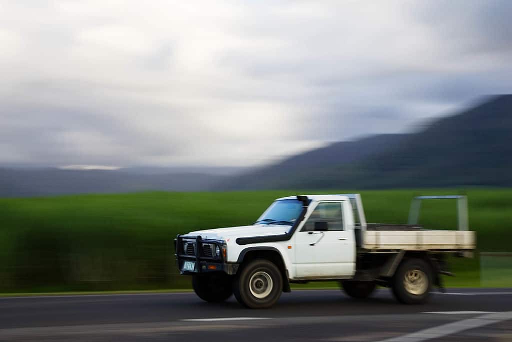 A pickup truck, or ute, driving along the road with blurred fields and mountains in the background.
