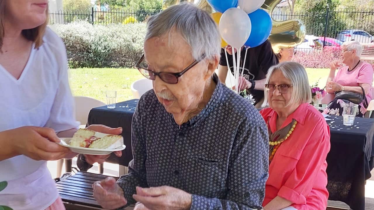 An elderly man being given a slice of cake
