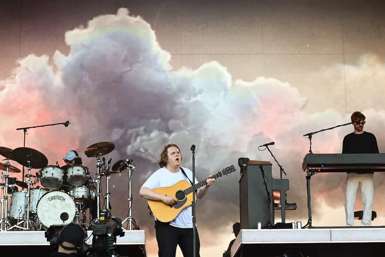 Lewis Capaldi sings on stage while his band plays.