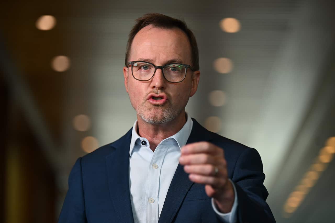A man in a suit raises his hand as he speaks