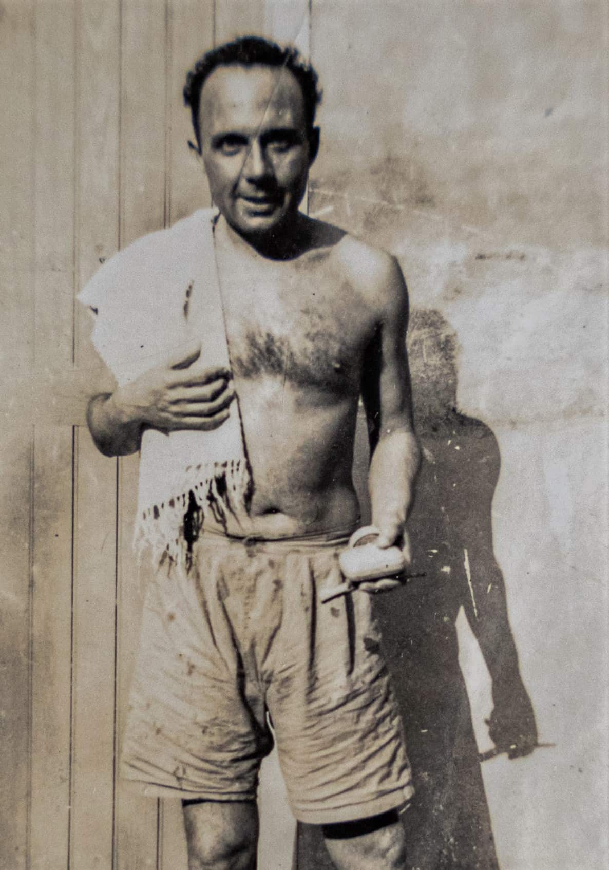 A sepia photo of a man in shorts standing against a wall.