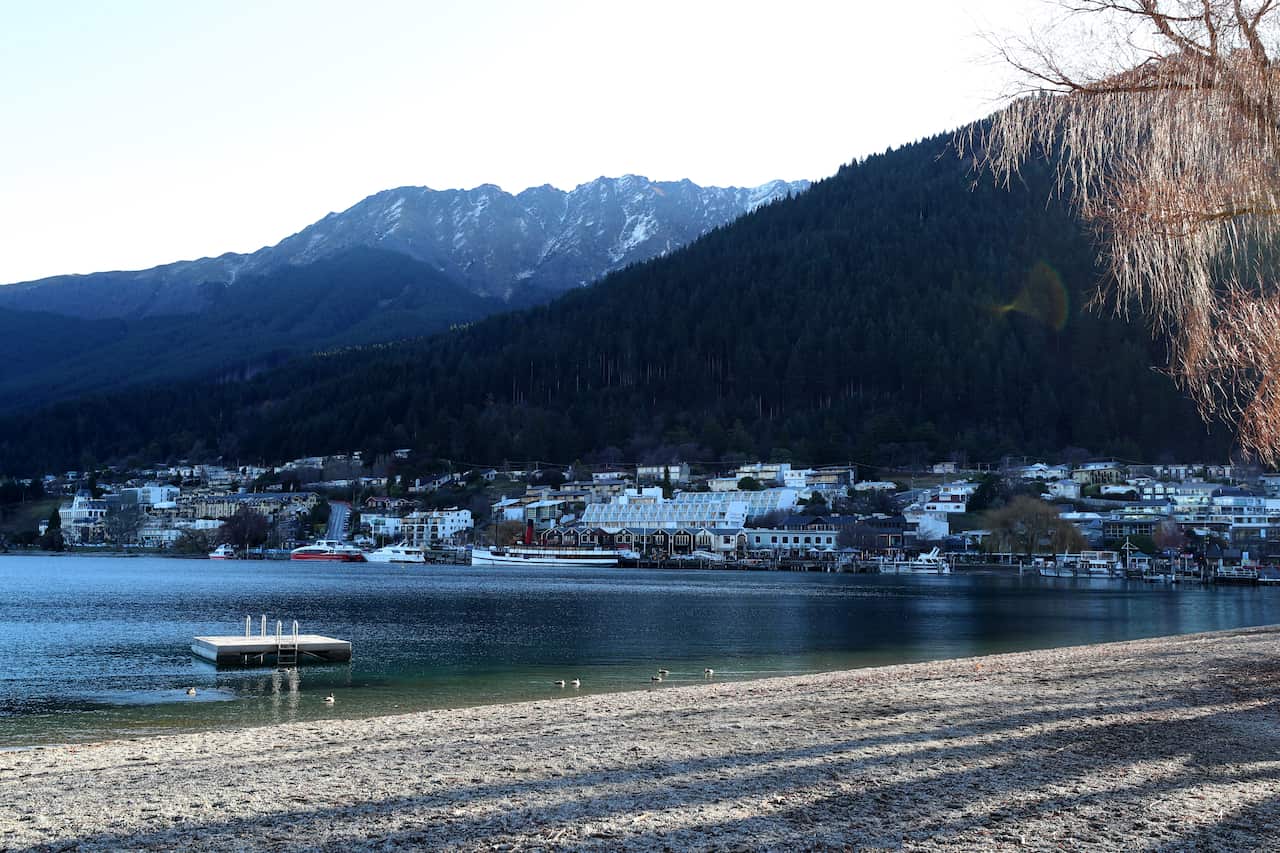 The shore of a lake, with houses and boats along the water's edge in the distance.