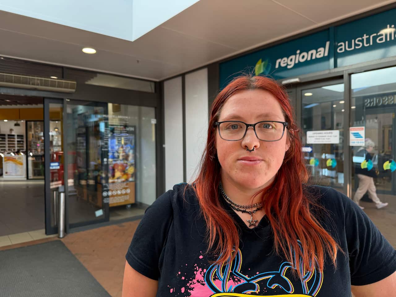 A person with dyed long red hair wearing glasses and a nose ring