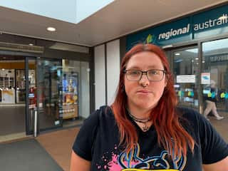A person with dyed long red hair wearing glasses and a nose ring