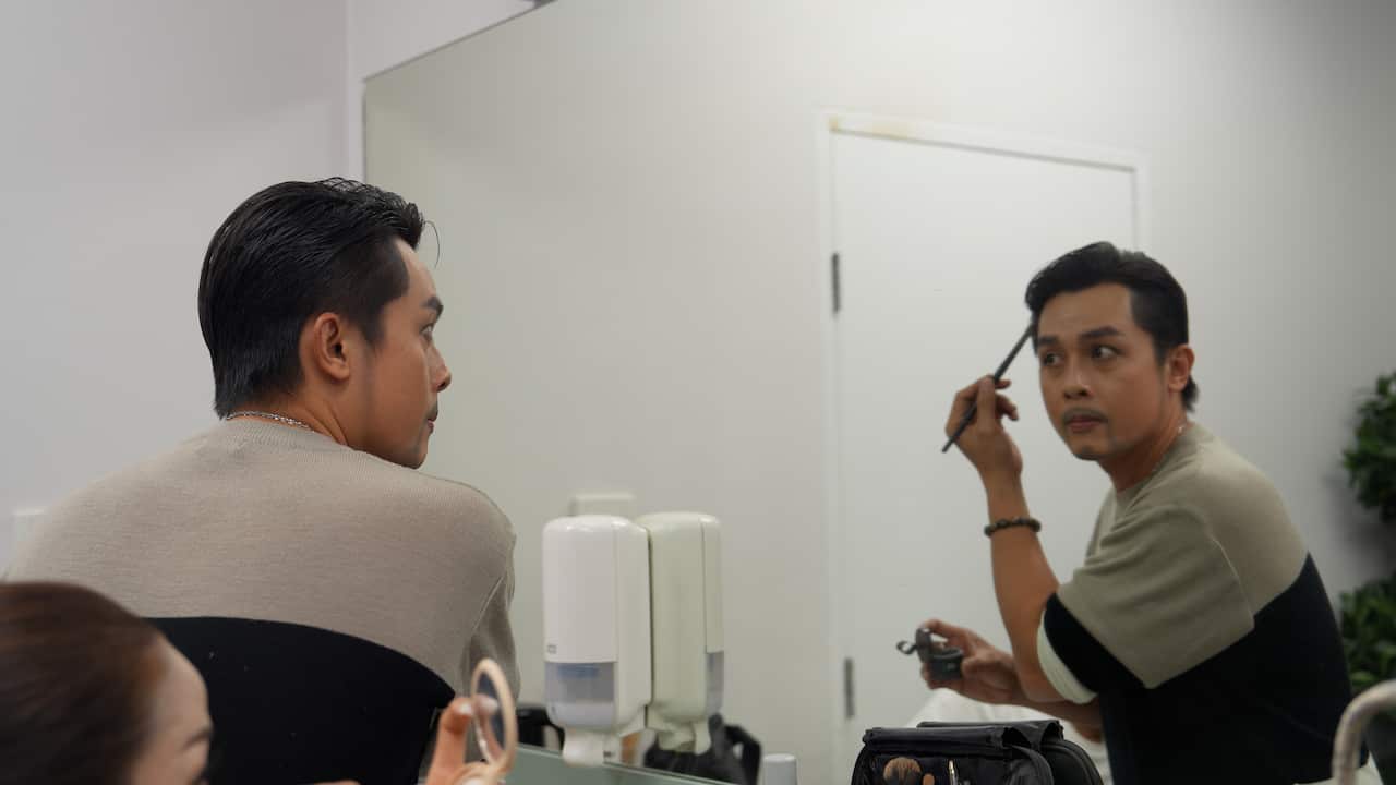Diễn viên Hòa Hiệp tự hóa trang trước giờ diễn, một phần công việc mỗi nghệ sĩ phải thành thạo để giữ đúng diện mạo nhân vật. Nguồn: Phương Linh / SBS Tiếng Việt