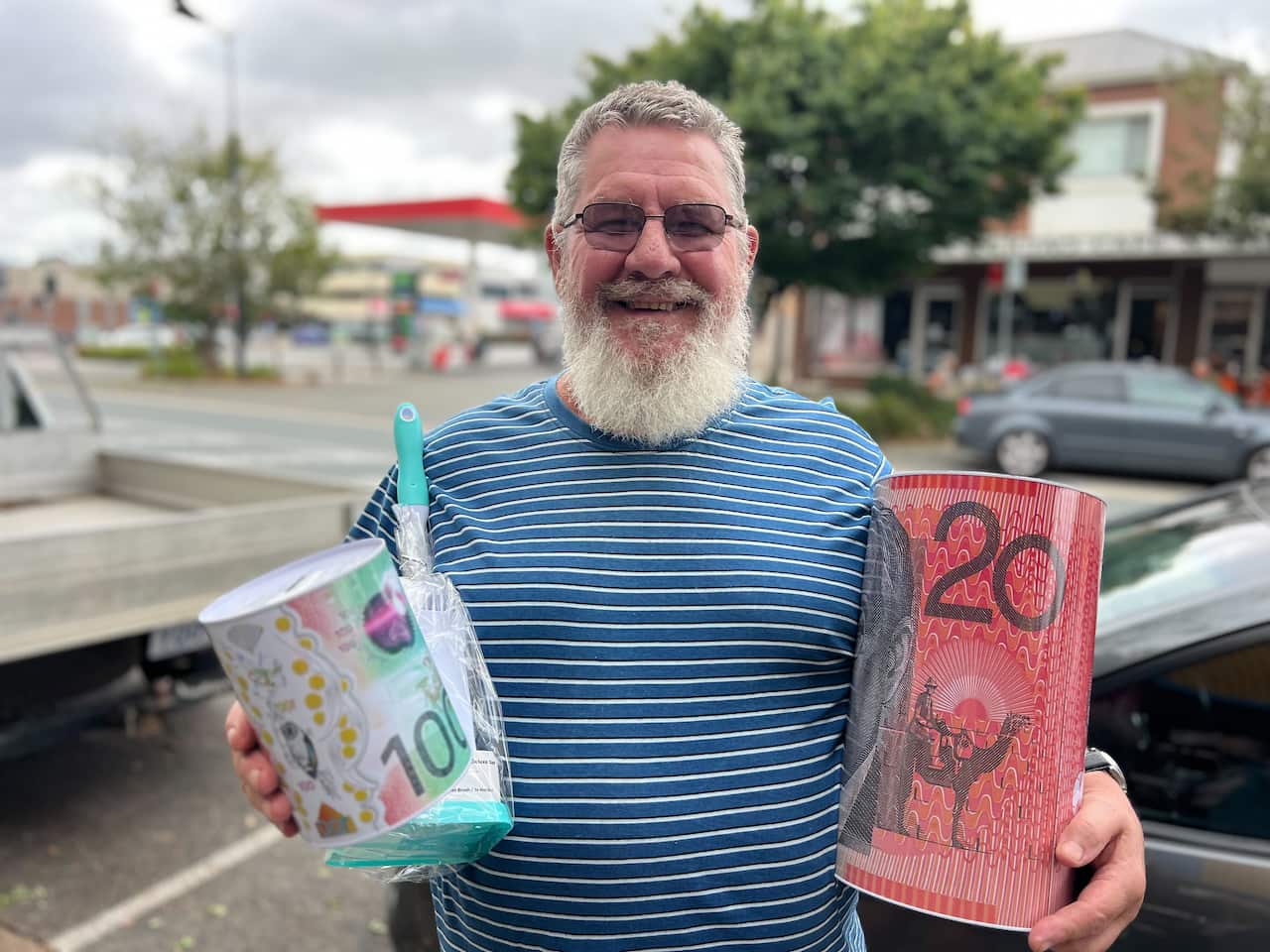 A man in a striped shirt holds two piggy banks smiling at the camera