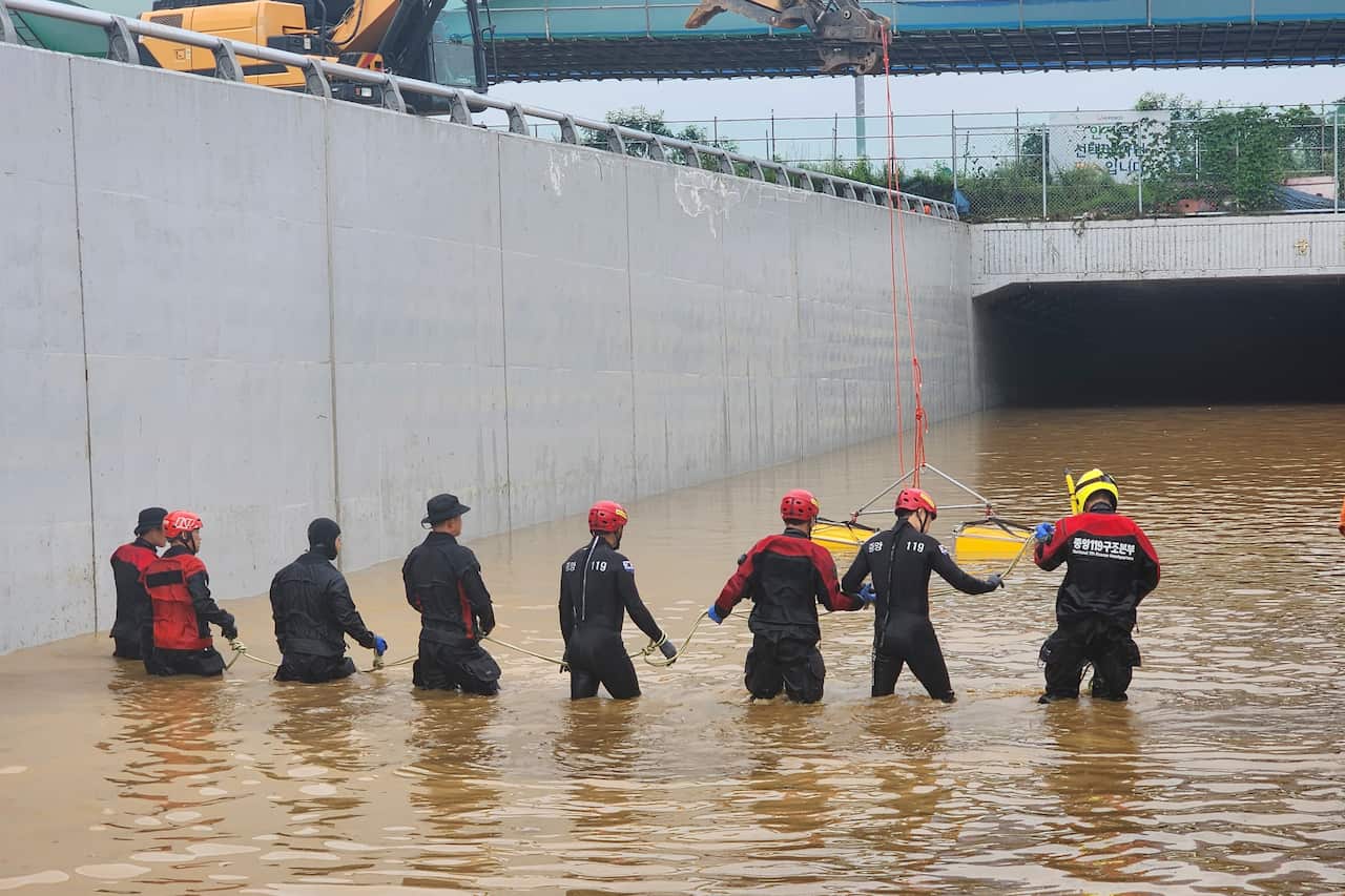 A search and rescue team wearing wetsuits wades through thigh-deep water towards a tunnel