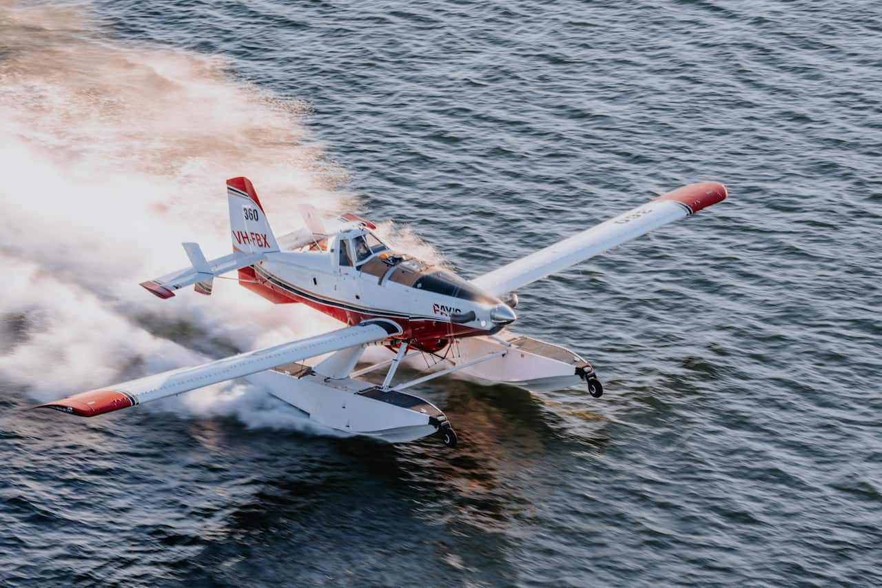 A Fire Boss plane lands on the water with its white and red body and a jet of water behind it