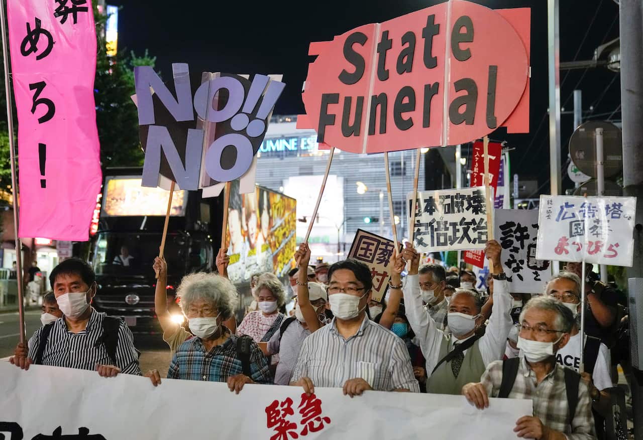 Protesters hold signs on a Japanese city street at night.