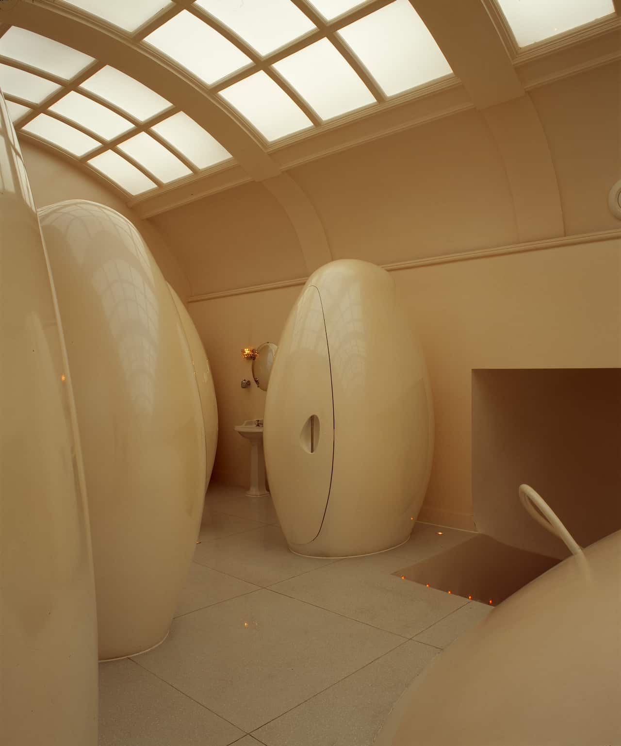 White egg-shaped pod toilets in a restroom inside a building with a glass panel ceiling.