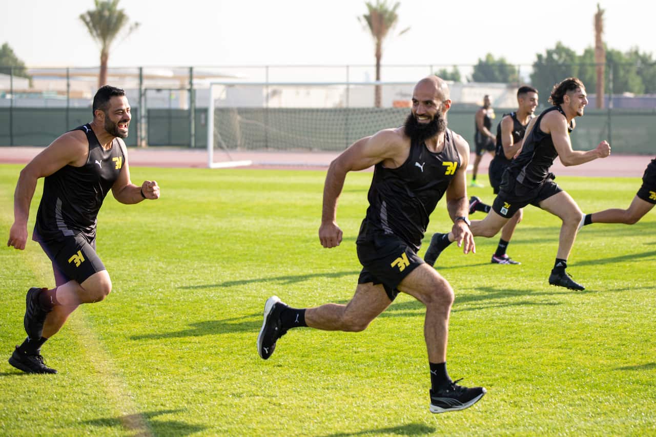 Bachar Houli is smiling while running on a field looking behind his shoulder with other young men. 