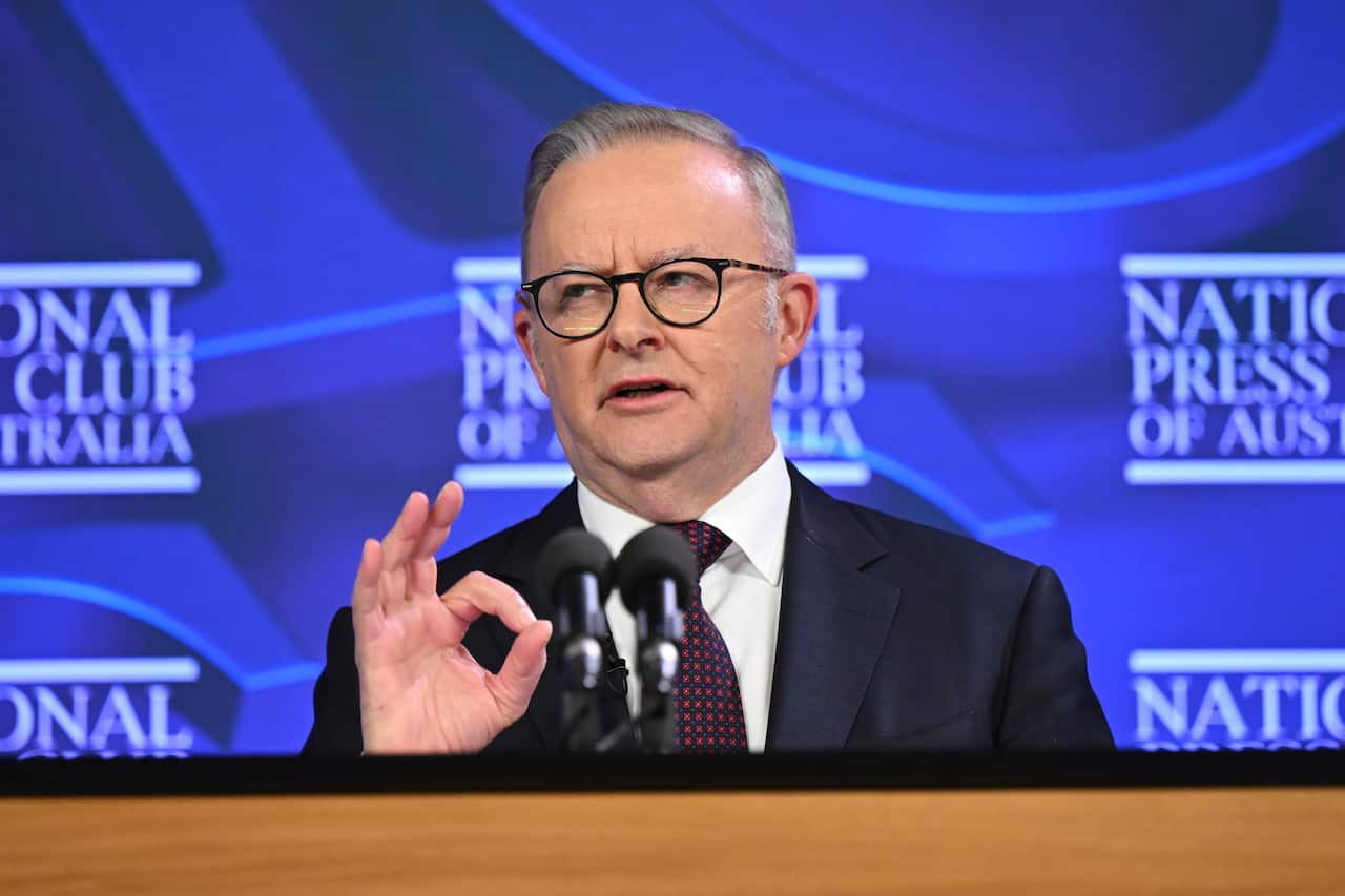 A middle-aged white man wearing a dark suit and lectern speaking before a lectern 