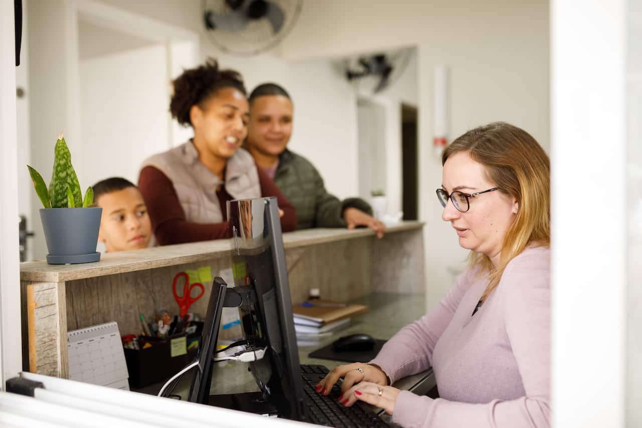 A family waiting at the counter while a receptionist types on her computer.