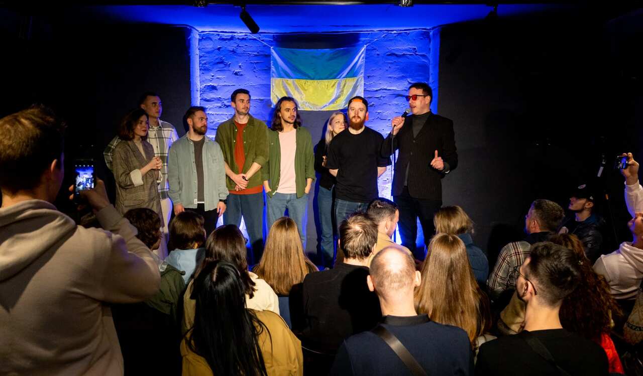 A group of people standing on a small stage in front of a Ukrainian flag