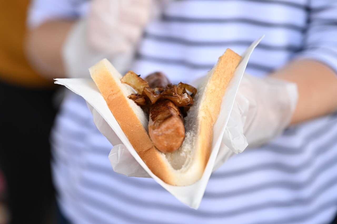 A woman holding a sausage in white bread with onions on top.