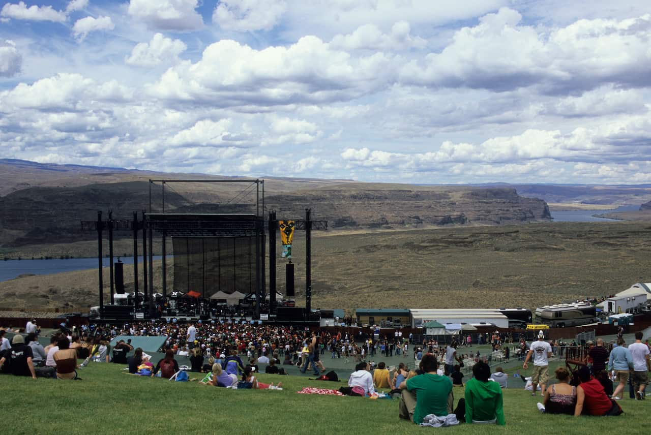 people sit in front of a stage in a field. 