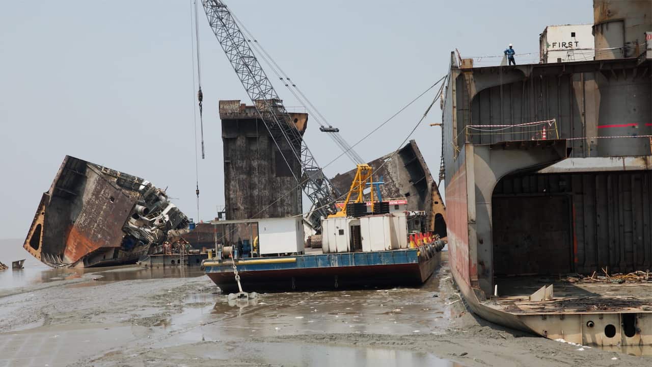 Broken carcasses of old ships lie beached in the mid next to a platform with a crane