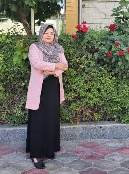 A woman in a pink cardigan and head scarf standing in a courtyard.