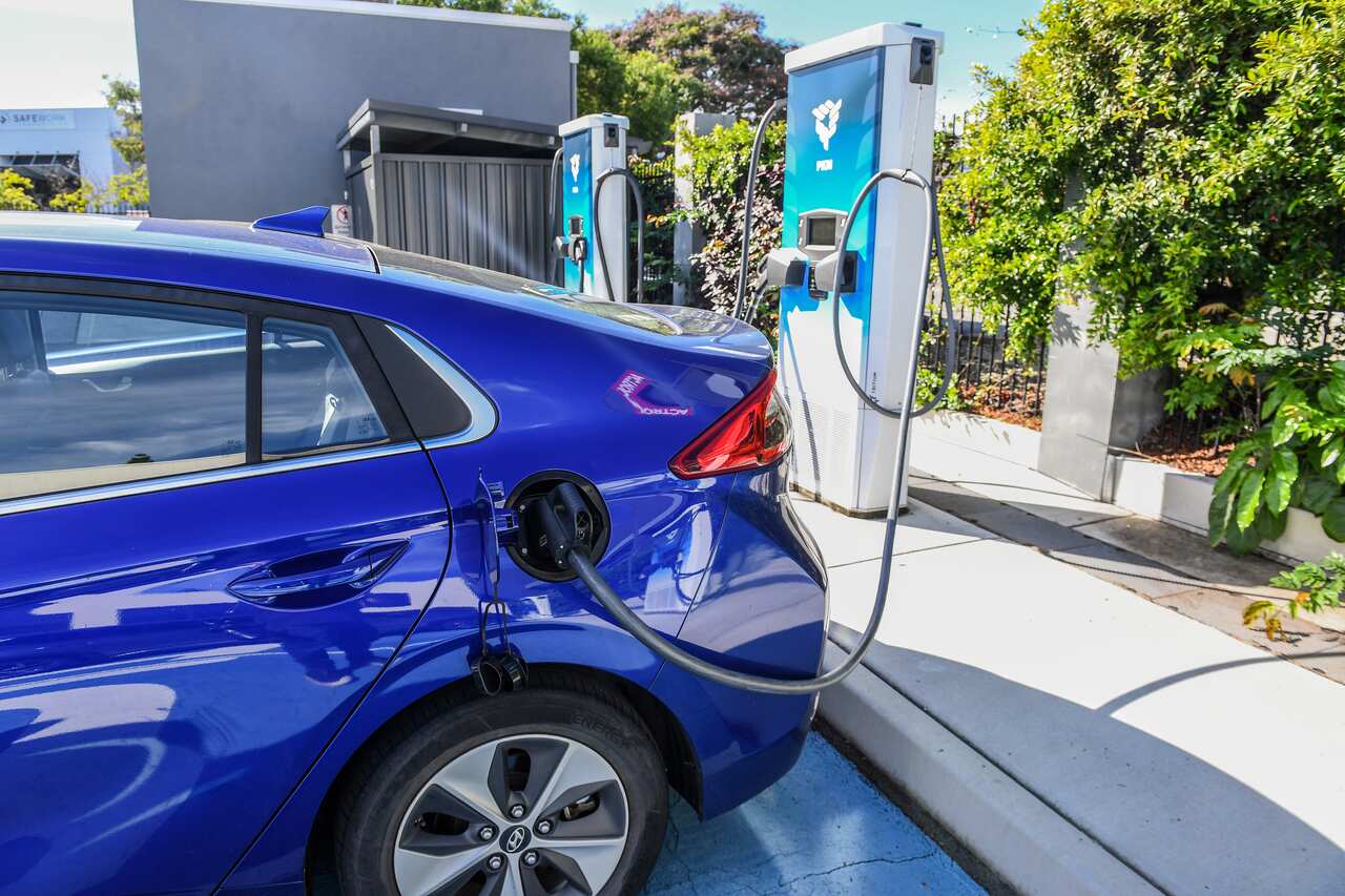 The back half of a blue sedan, with a charger connecting the car to a charging station.
