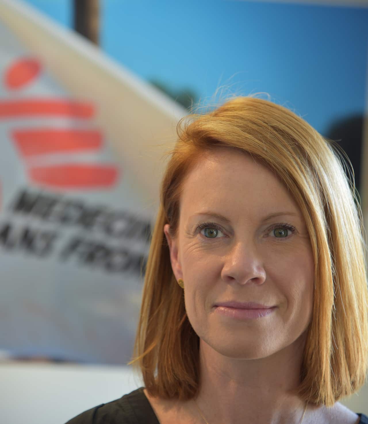 A woman in front of a blurred Médecins Sans Frontières flag.