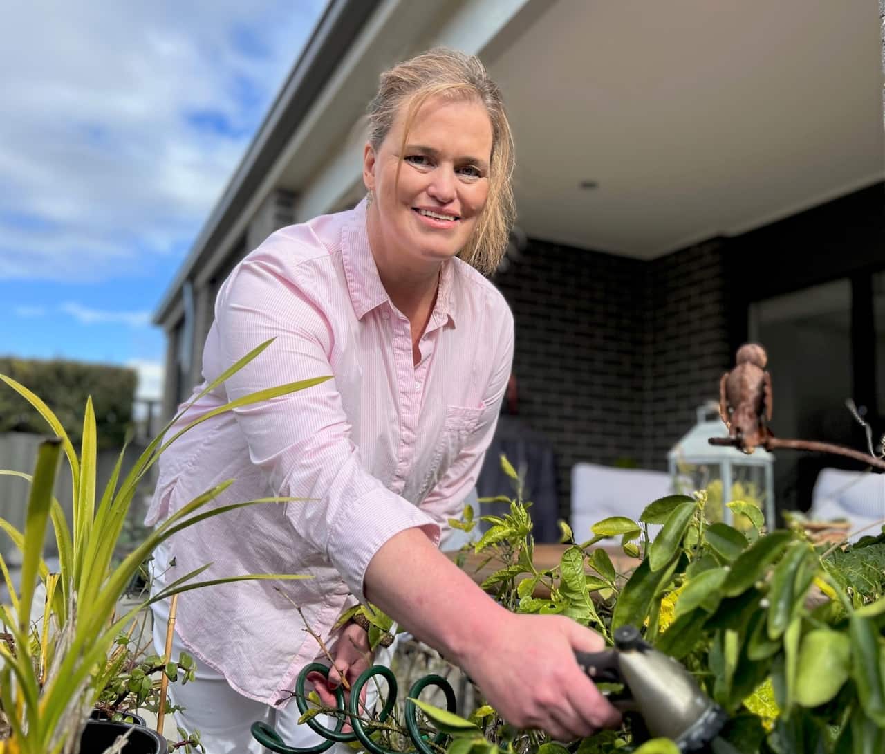 A woman wearing a pink shirt leans into a garden holding a hose.