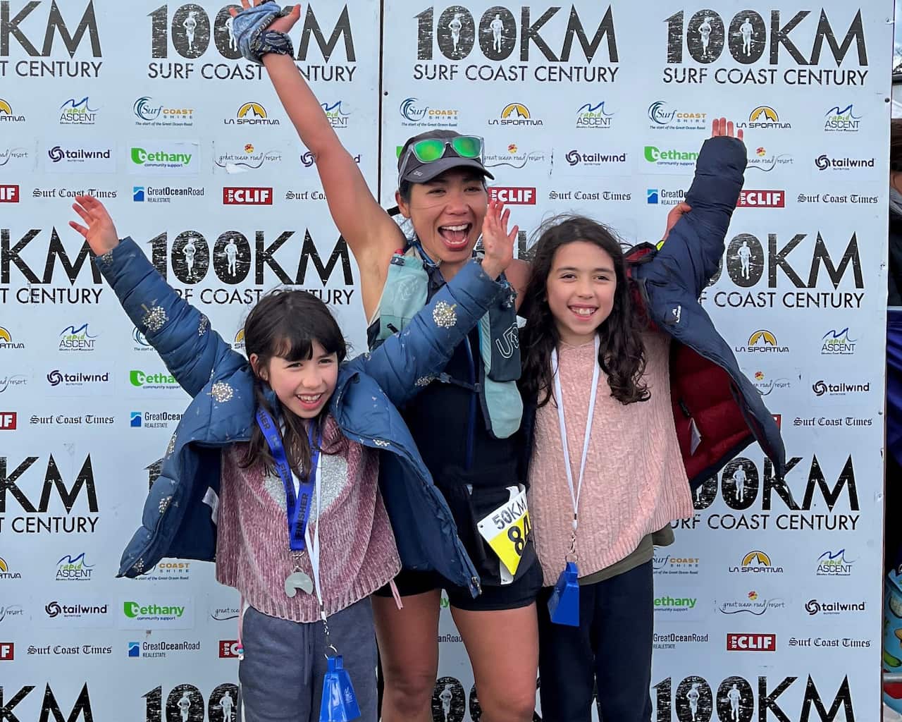 A mother and her two daughters look happy, with their hands up above their heads.