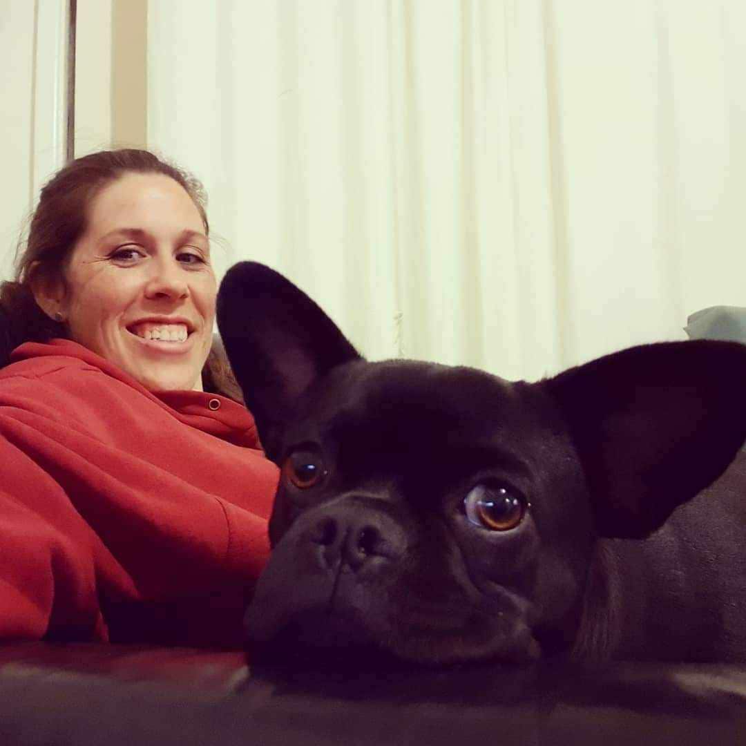 A woman in a red hoodie sits on a couch with a black dog