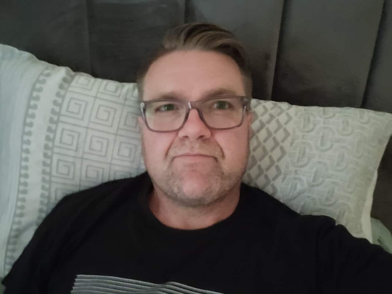 A man wearing glasses laying on a bed