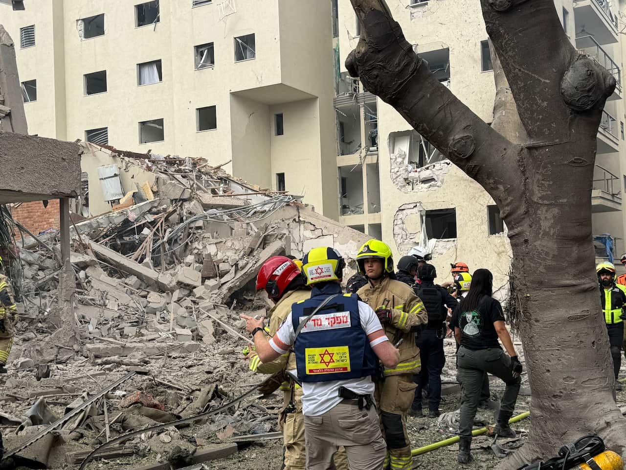 Rescue workers stand amid the debris of a damaged building.