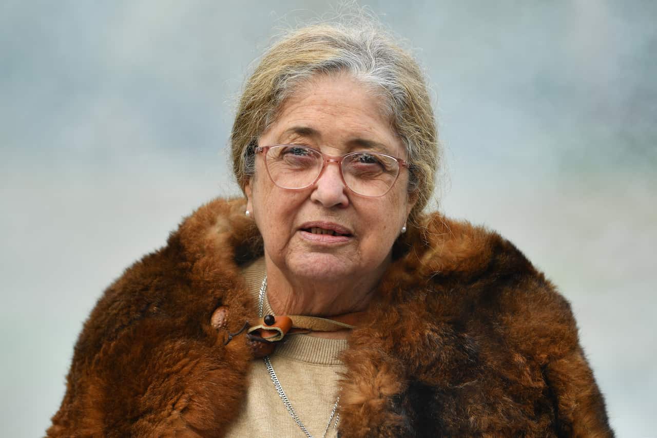 A woman in a fur coat addresses the media with a serious expression.