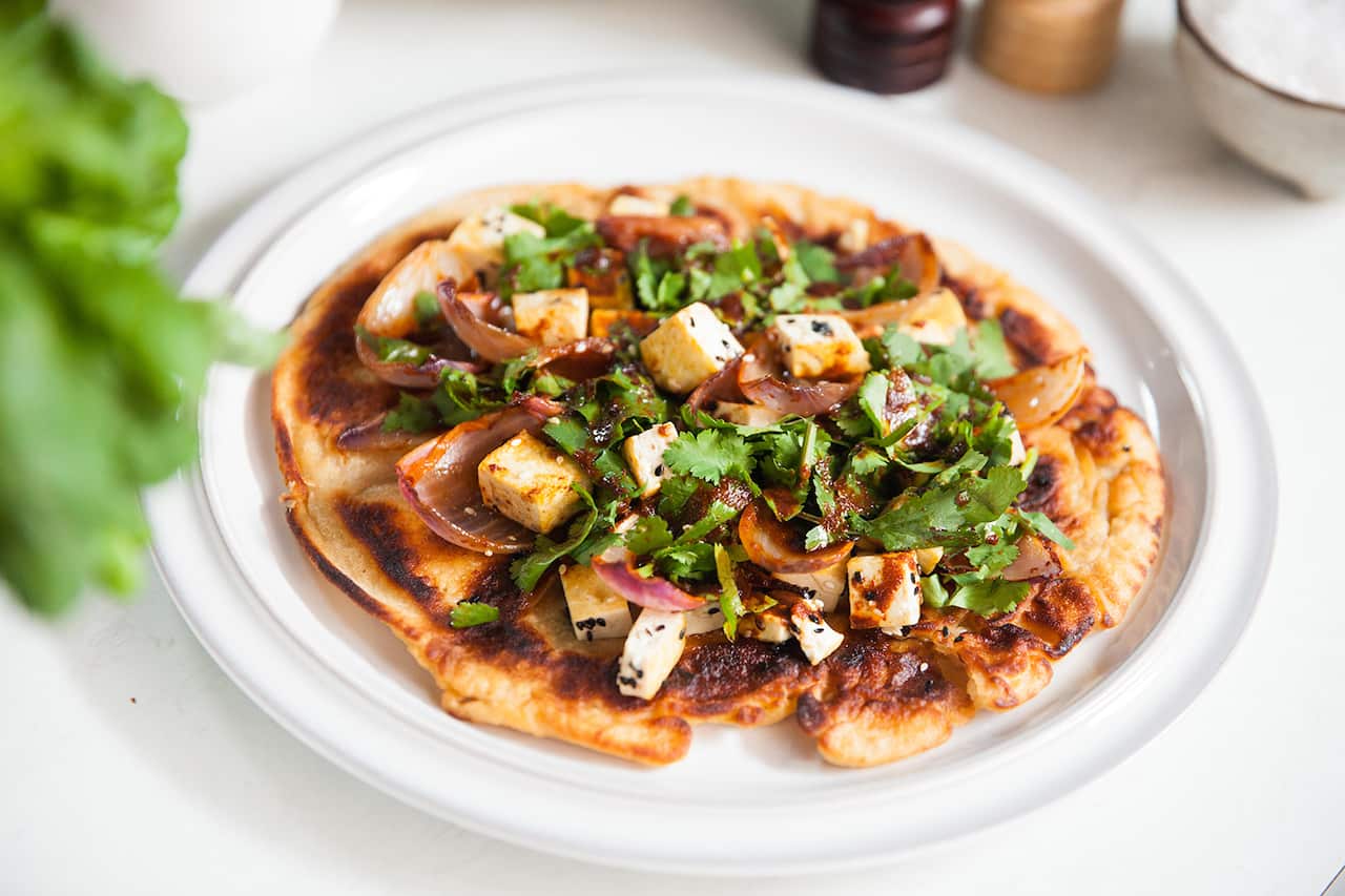 A round of bread is topped with tofu, cooked onion and fresh coriander.