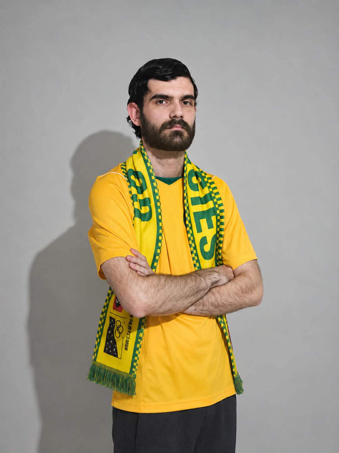 A young man wearing a Socceroos shirt and scarf with his arms crossed