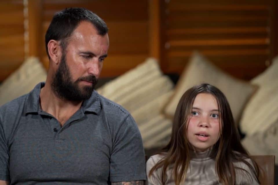 A man and a young girl sitting down and speaking to a camera