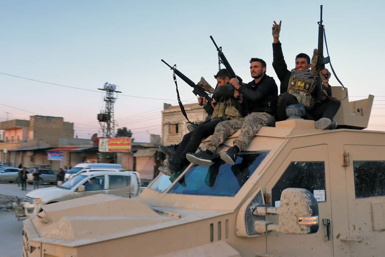 Three men in military fatigues sit on the roof of a Humvee brandishing machine guns. 