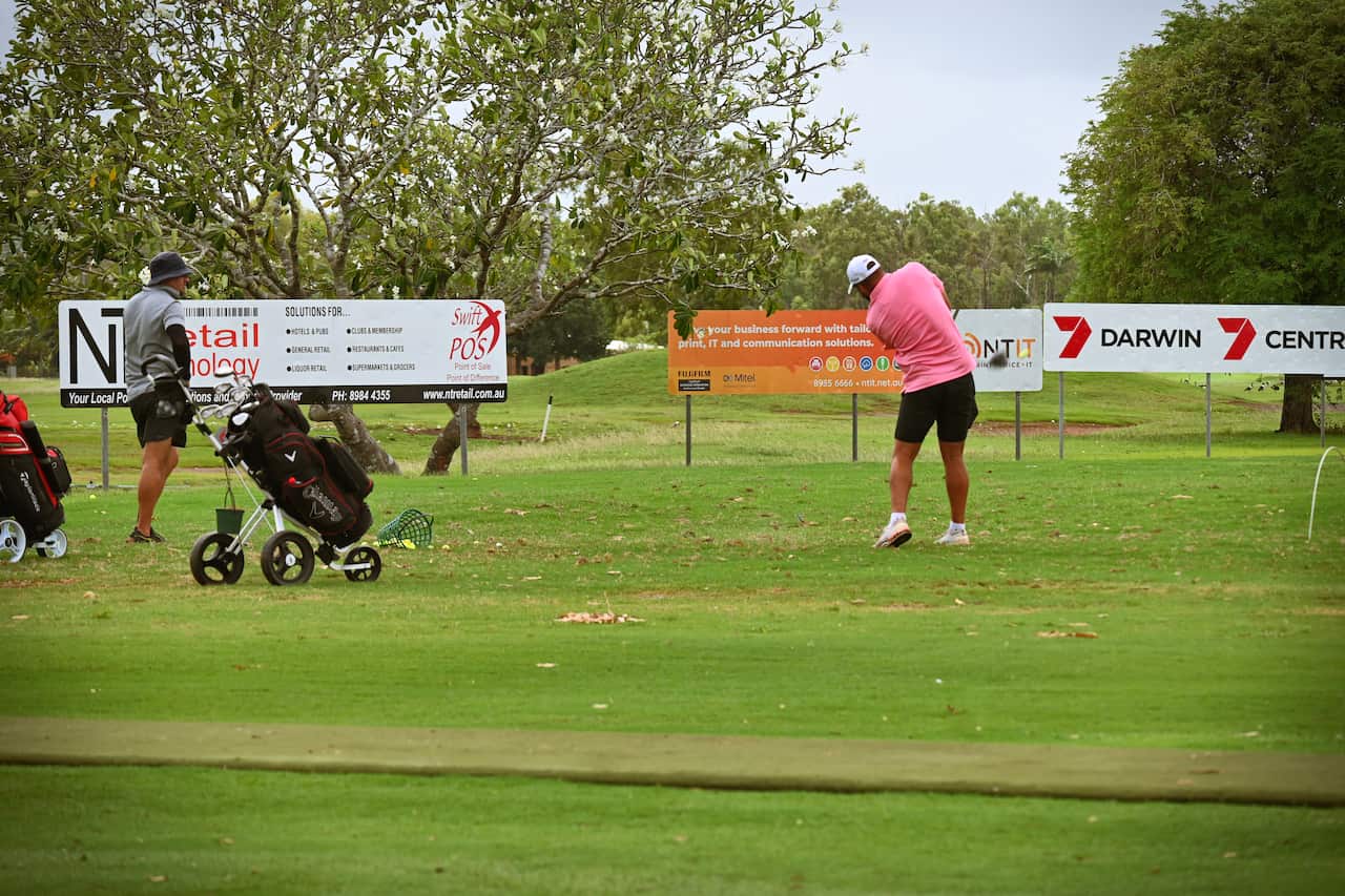 A male golfer in a pink shirt hits a ball off the driving range at Darwin Golf Club