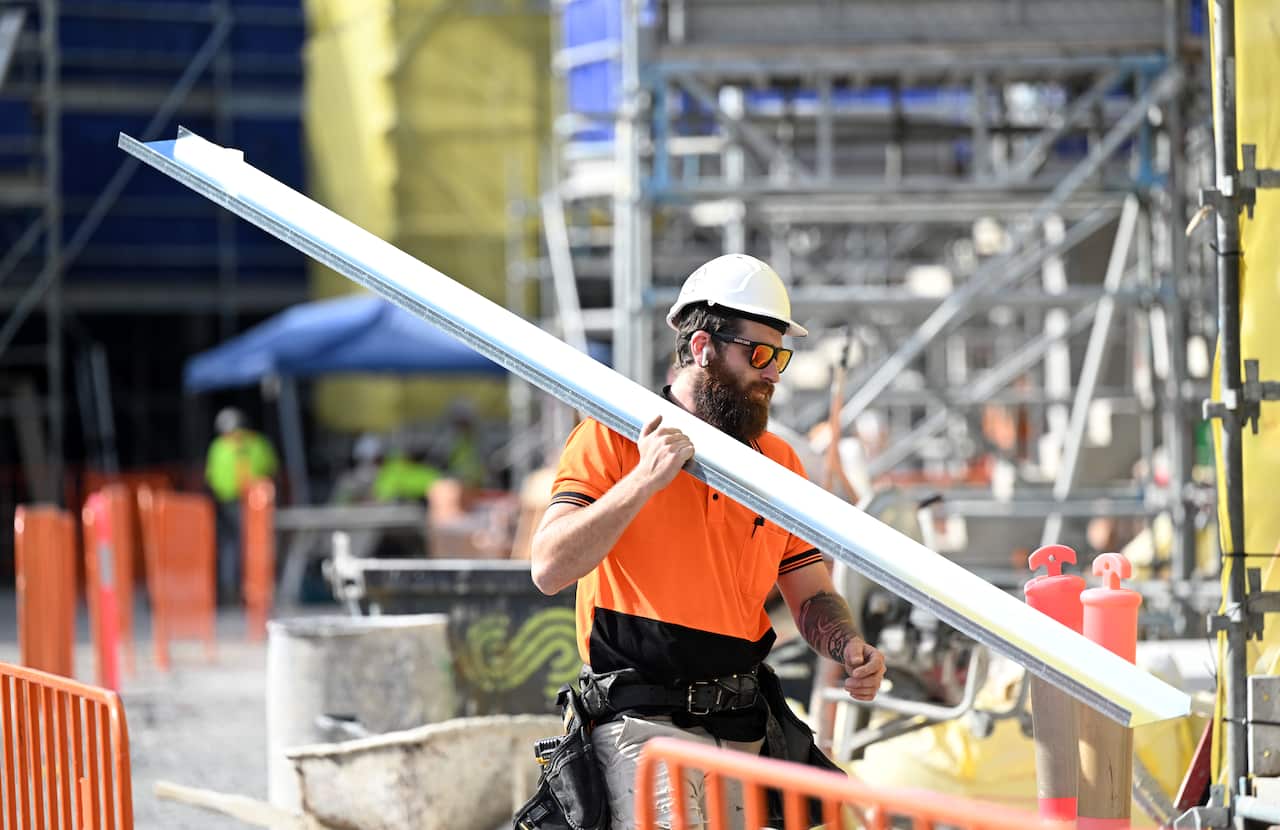 A man in high-vis shirt and helmet holds a piece of metal gutter.